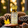 Golden Taiba Attar bottle surrounded by pinecones and autumn leaves, showcasing fragrance for men and women by Jigri.